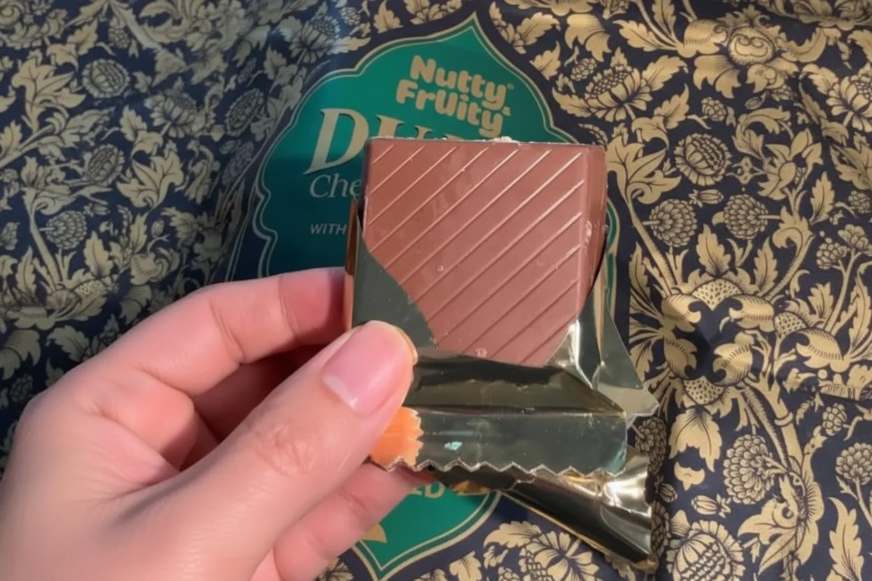 Hand holding a piece of Nutty & Fruity Dubai Chocolate Bar, showcasing pistachio milk chocolate bars in gold wrapping.