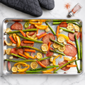 Heavy duty aluminum sheet pans filled with roasted vegetables and meat, showcasing versatility and durability.
